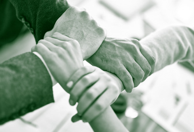 Manos de cuatro personas entrelazadas simbolizando cooperación y trabajo en equipo.